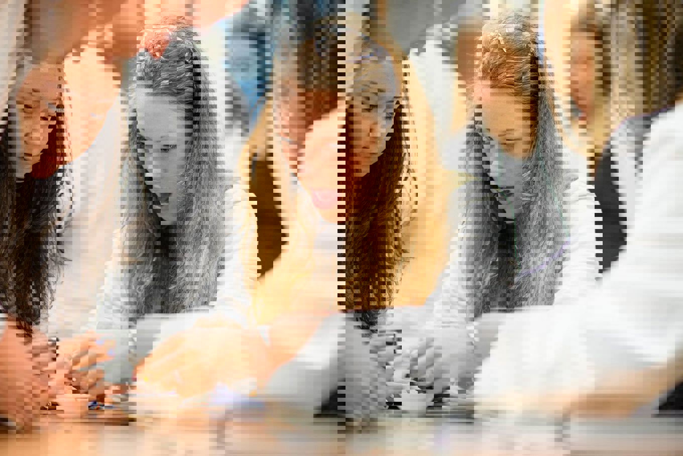 Engasjert jente gjør kjemiforsøk sammen med medelever i hvite frakker på kjemisalen.